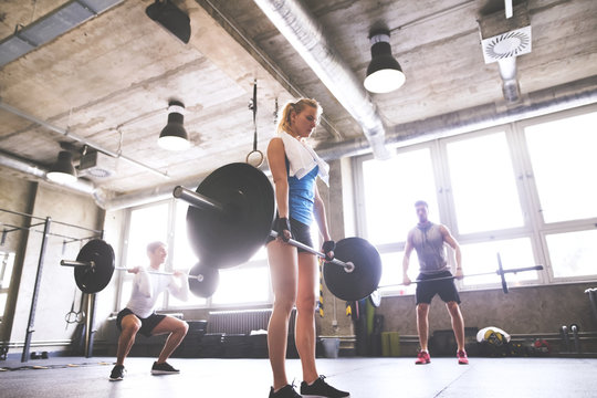 Young woman with training partners lifting barbell in gym