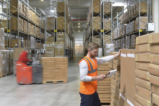 Man with clipboard in factory hall and moving forklift