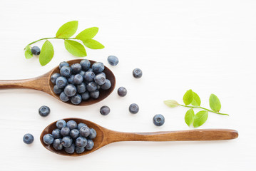 Fresh  blueberries in a wooden spoons on a white surface of a table. Closeup, top view.