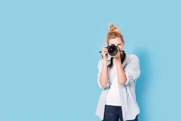 Foto op Plexiglas Young blonde photographer is taking a photo. Model isolated on a blue background with copy space © Daniel Krasoń