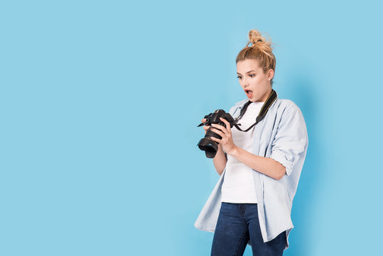 Young blonde photographer is shocked about photo she made. Model isolated on a blue background with copy space