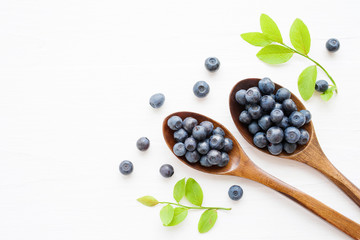 Fresh  blueberries in a wooden spoons on a white surface of a table. Closeup, top view.