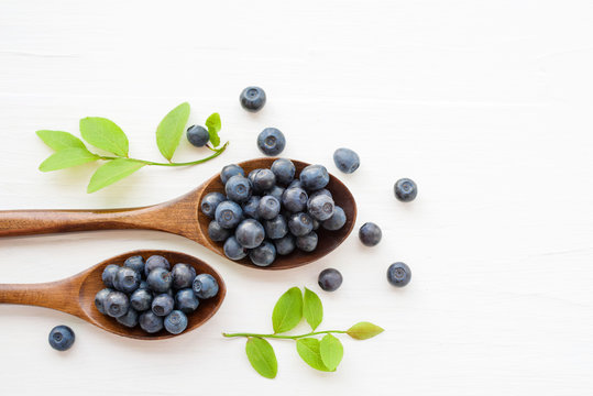 Fresh  blueberries in a wooden spoons on a white surface of a table. Closeup, top view.