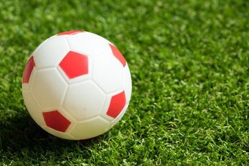 Fototapeta premium Toy red and white color football on artificial green grass background