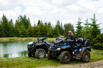 A happy woman riding a quad bike near a lake in the mountains