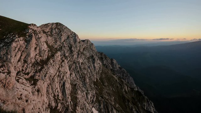 Stunning sunset in Piatra Craiului Mountains with red horizon in the background and grey impressive cliff in foreground.  Romania, 4k timelapse.