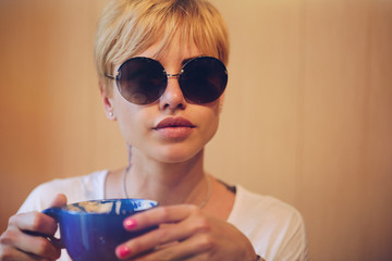 Girl with glasses with coffee/ Beautiful girl with short hair in sunny round glasses with a big blue mug of coffee.