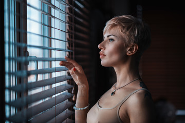 girl at the window with jalousie/ beautiful girl at the window of the house looks out between the...
