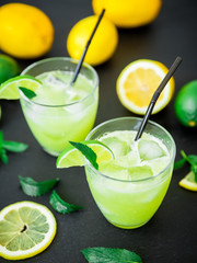 Fresh citrus lemonade with limes and lemons in glasses on black