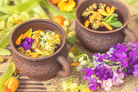 Two ceramic cups of healthy herbal tea with decoction of dry and fresh flowers on dark aged rustic wooden background. Shallow depth of field.