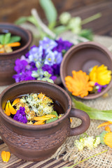 Obraz na płótnie Canvas Two ceramic cups of healthy herbal tea with decoction of dry and fresh flowers on dark aged rustic wooden background. Shallow depth of field.