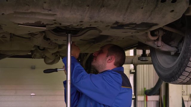 Car mechanic in robe inspects the body of the car on the car lift in garge close-up. 4k