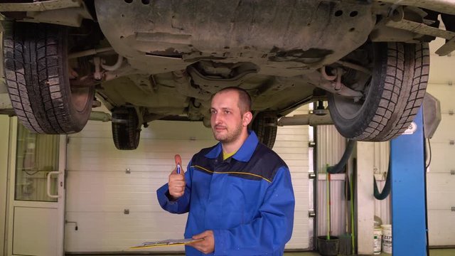 Auto mechanic in blue overalls fills the papers on the basis of car inspection in garge.