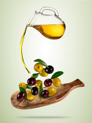 Olive oil with flying olives in wooden bowl
