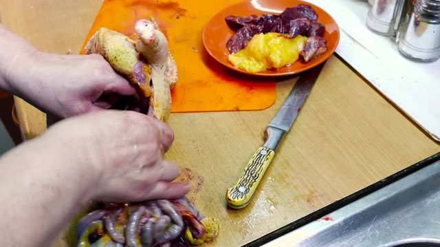 A woman is carving a bird on a cutting wooden board at home in the kitchen. She gets inedible guts. Edible viscera are located in an orange plate