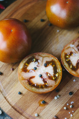 Halves of Kumato tomatoes on wooden board surrounded by vegetables and spices.