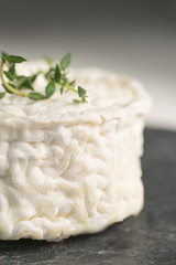 Close-up of goat aged cheese with a branch of thyme on a dark stone background
