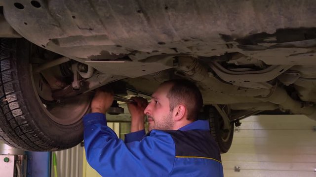 Auto mechanic in blue robe repairs car suspension in garge close-up.