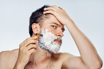 Young guy with a beard on a light background shaves