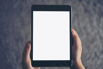 Mockup image of a woman sitting and holding black tablet pc with blank white screen with gray rug in background