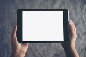 Mockup image of a woman sitting and holding black tablet pc with blank white screen with gray rug in background