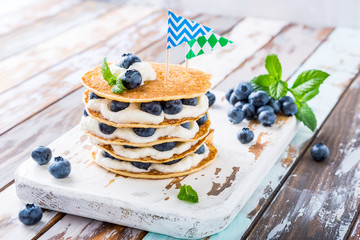 Small cake made of pancakes with cream and blueberries on old white wooden board. Children's party background. Healthy food concept, copy space.