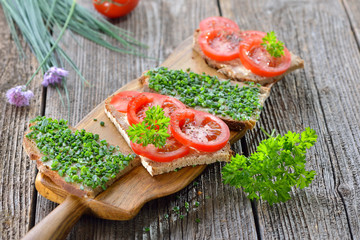 Vegetarische Brotzeit: Bauernbrote mit frischem Schnittlauch und Tomaten auf  Brotzeitbrett serviert – Vegetarian snack: Slices of farmhouse bread with fresh chives and tomatoes on a wooden board