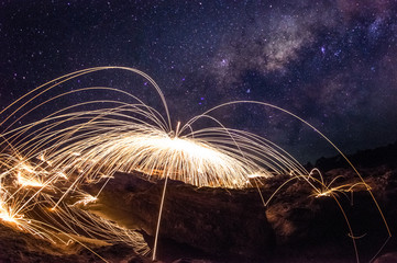 Amazing fireworks, Burning and spinning steel wool on the rock, Showers of hot glowing sparks, Long exposure photo background, Grand canyon of Thailand, The Milky Way galaxy pointing on a bright star.