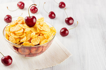 Breakfast with golden corn flakes, ripe cherries on white wood board.