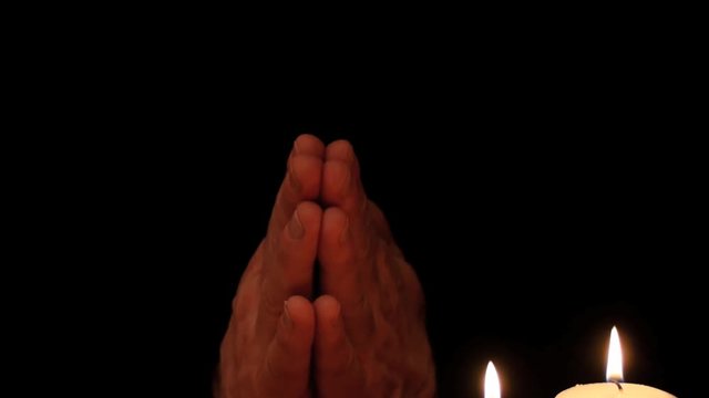 Prayer hands on black background with candles closeup smooth zoom