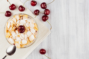 Breakfast with golden corn flakes, ripe cherry, powdered sugar on white wood board top view, copy space.
