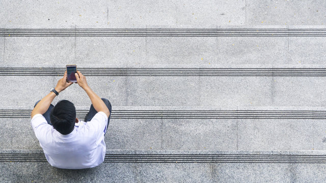 the top aerial view of the man in white shirt uses mobile phone and sits on the pedestrian concrete walk way at stair public.