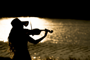Woman playing violin at the river on sunset,silhouette and blur photography.