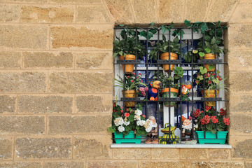 Stone wall with a window decorated with pots, flowers and colorful ornaments, located in the city of Cadiz, Spain