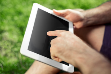 Young hipster boy sitting in the park and using modern digital tablet
