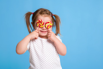Beautiful little female child holding huge lollipop spiral candy smiling happy isolated on blue background.