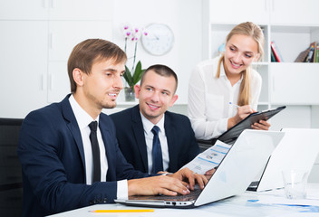 Portrait of three cheerful business colleagues discussing paper work with document in hands in office.  Focus on the left man