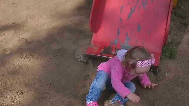 Little two year old blond girl in jeans plays in a children's park, children slide