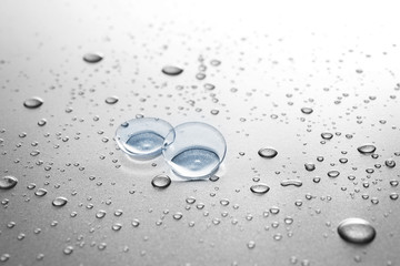 Contact lenses and drops of water on gray background