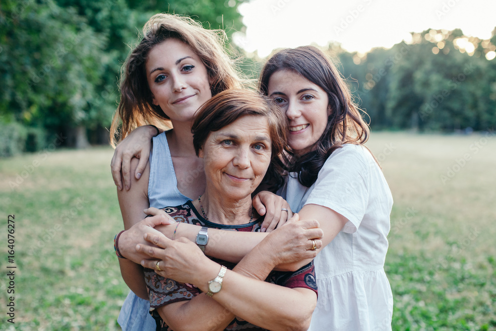 Wall mural mother and daughters embrace in a park at sunset on a summer evening