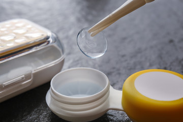 Tweezers with contact lens and plastic container on gray background