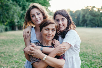Mother and daughters embrace in a park at sunset on a summer evening