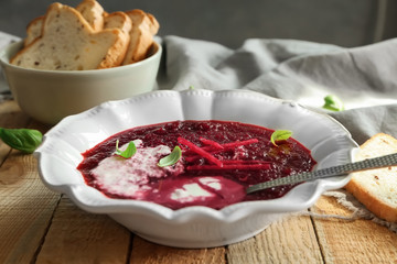 Delicious beet soup with sour cream and basil leaves on kitchen table