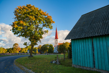 Bellfry and ancient Lutheran church in Kihelkonna, Saaremaa, Estonia. Early autumn sunny day. Village view with road, tree and barn