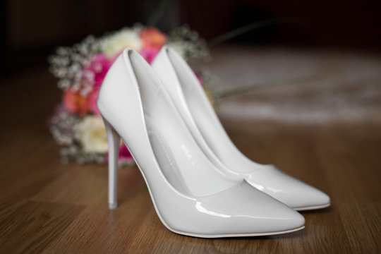 Wedding bouquet and white shoes stand on the floor before a window