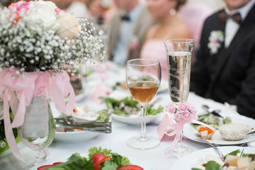 Champagne flutes decorated with roses stand before newlyweds