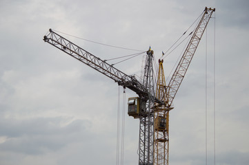 Fototapeta na wymiar Two construction cranes against a gray rainy sky background