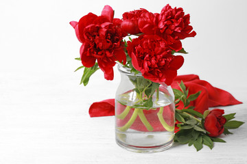 Glass vase with beautiful peonies on light background