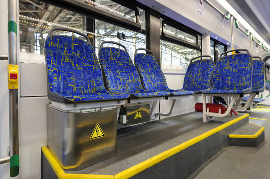 Modern tram inside, city transportation interior with blue seats in row, chrome handles for standing passengers, bright lights and air conditioner 