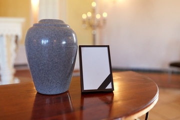photo frame with mourning ribbon and cremation urn - obrazy, fototapety, plakaty